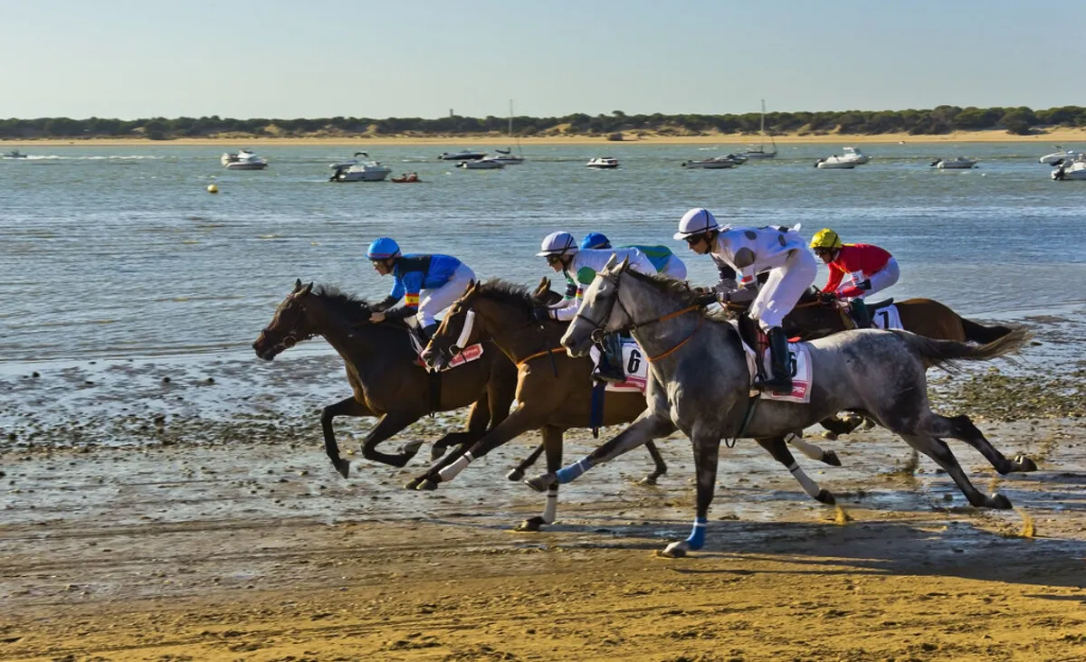 Una carrera de caballos en la playa con el mar y los veleros de fondo