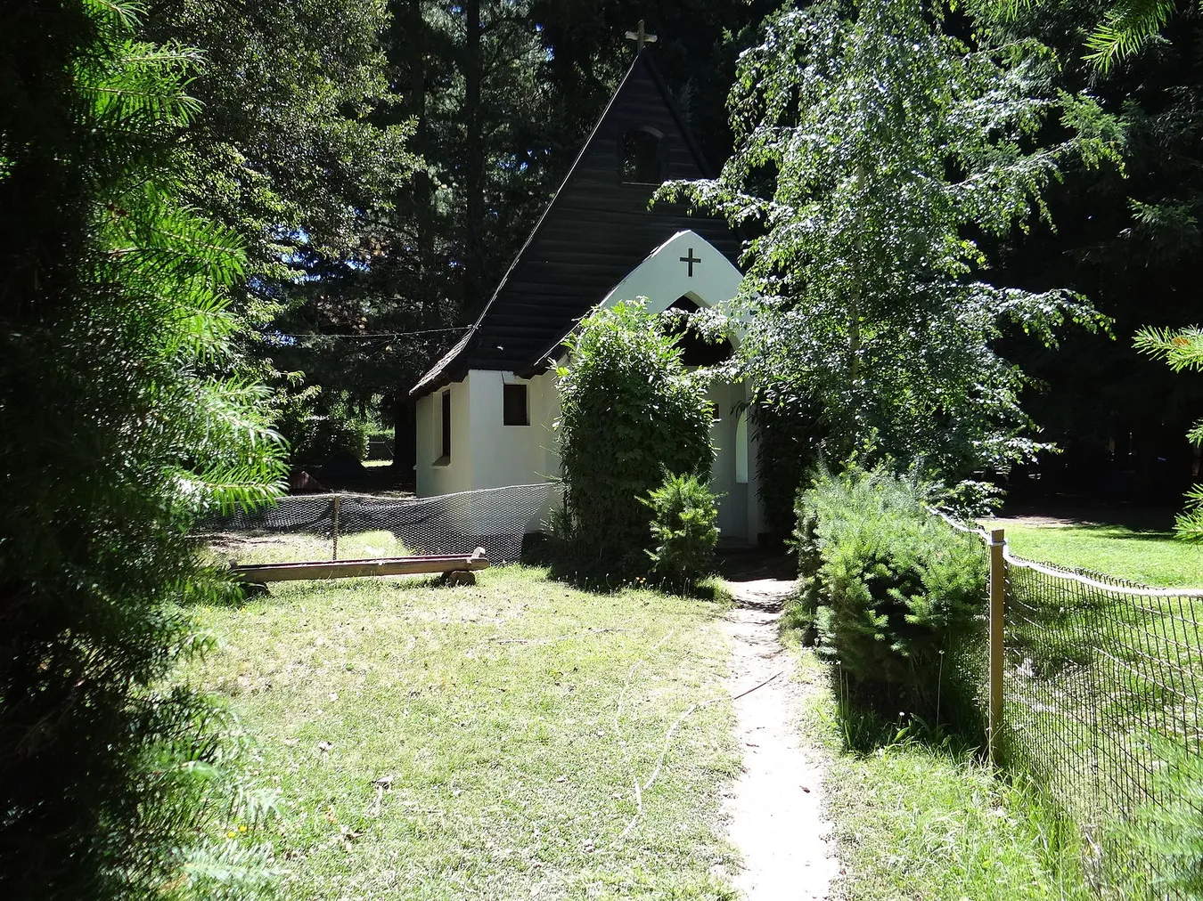 Una preciosa capilla blanca que se encuentra entre arboles y frondosa vegetación