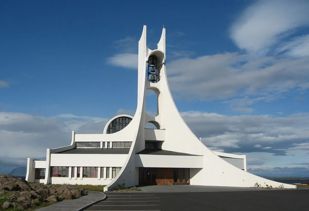 Iglesia de estilo modernista con estructura de hormigón de color blanco y con una pequeña puerta de madera.