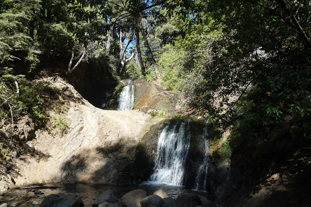 La cascada vista desde cerca con poca agua cayendo y el sol reflejado en la piedra