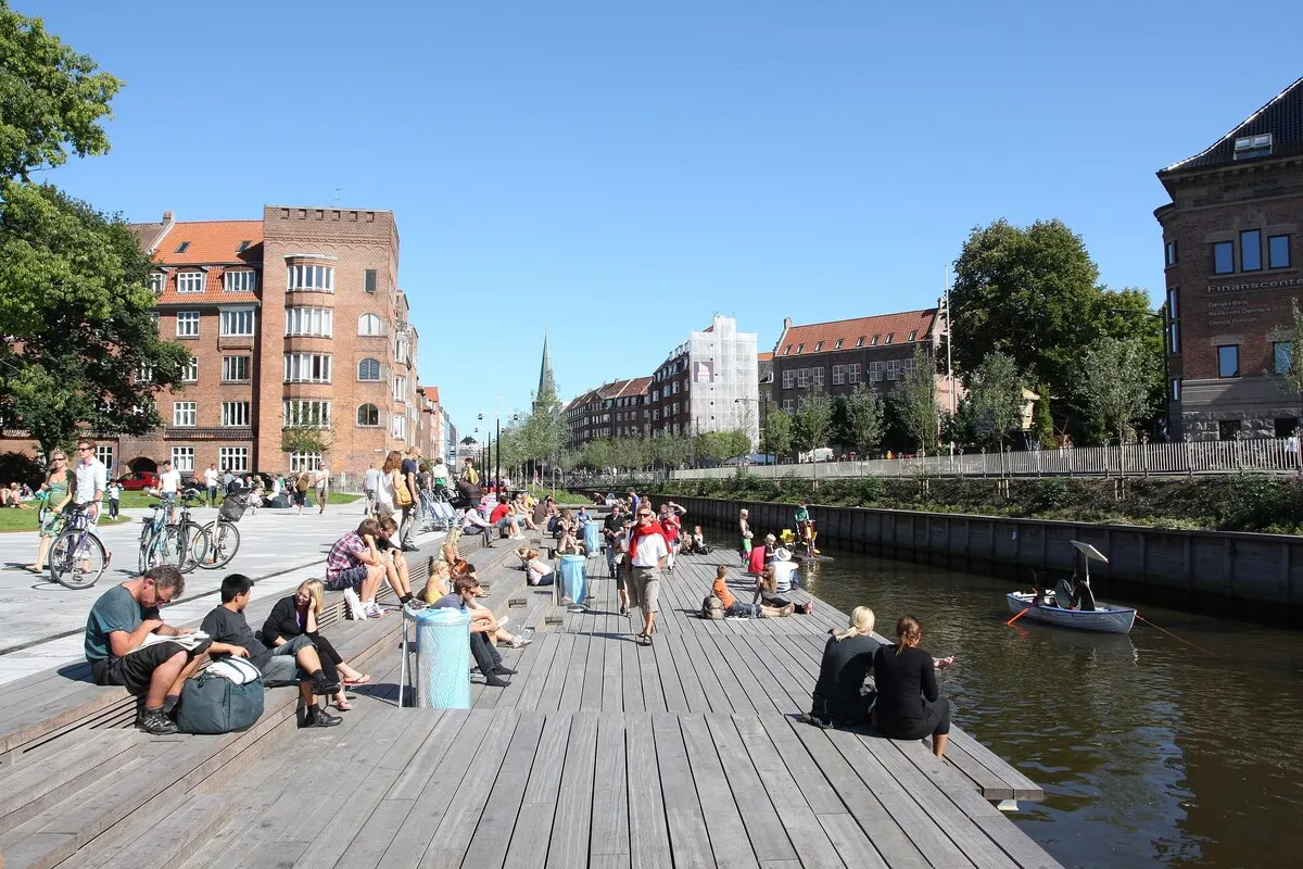 El paseo. peatonal al lado del rio con una barca navegando y gente paseando en bici y andando durante un día soleado