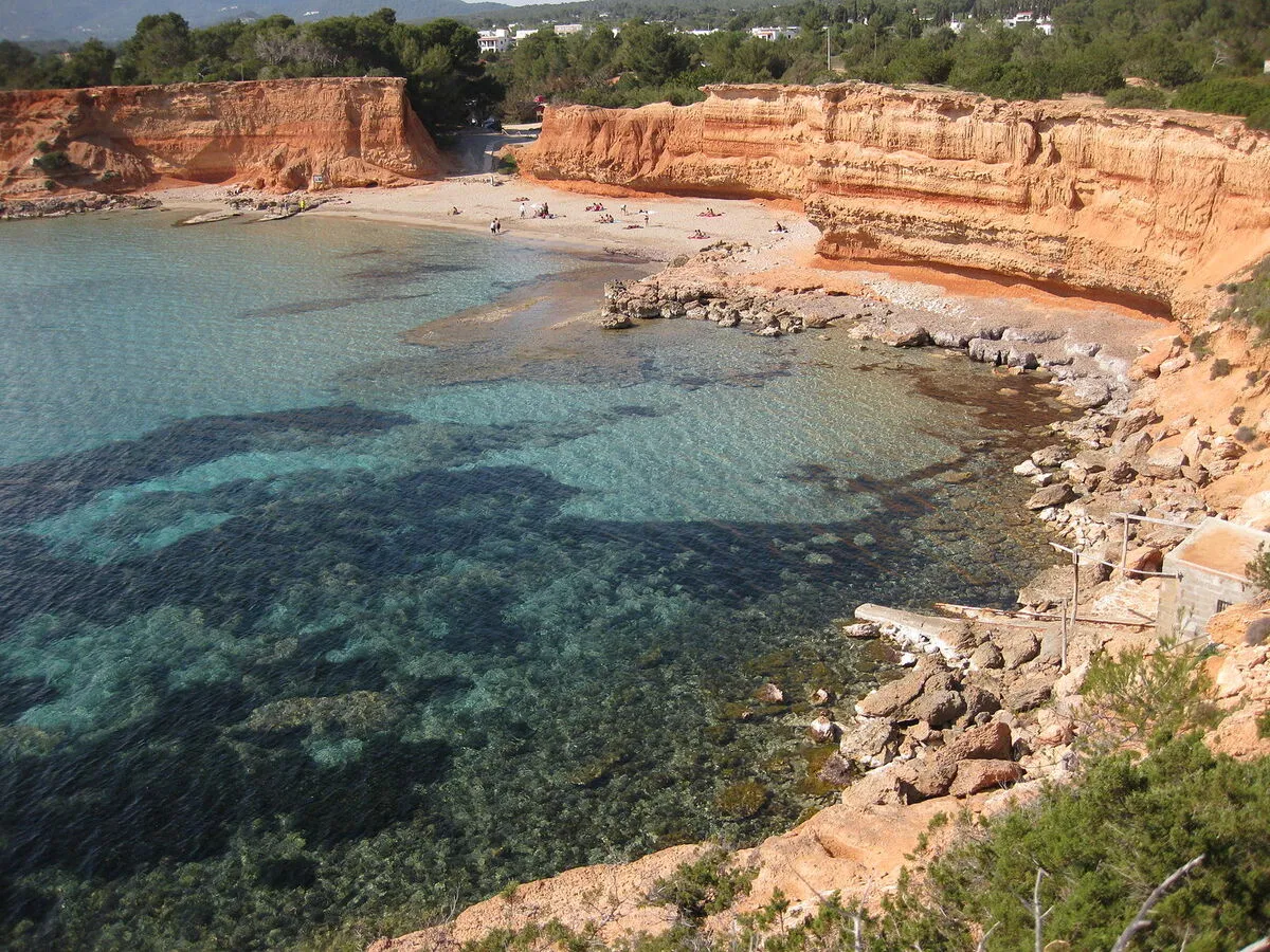 Panorámica de la playa con aguas cristalinas, arena roja y acantilados de piedra caliza