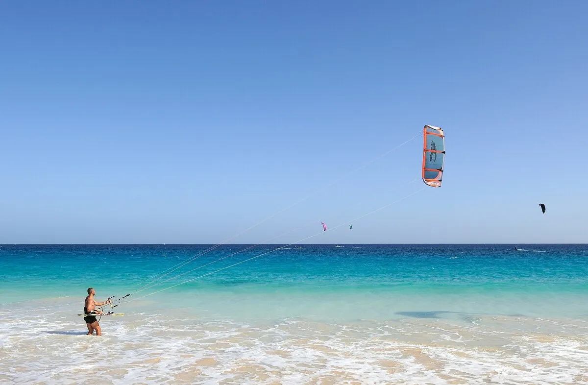 Mar color turquesa con un bañista en la orilla, preparado para hacer windsurf.