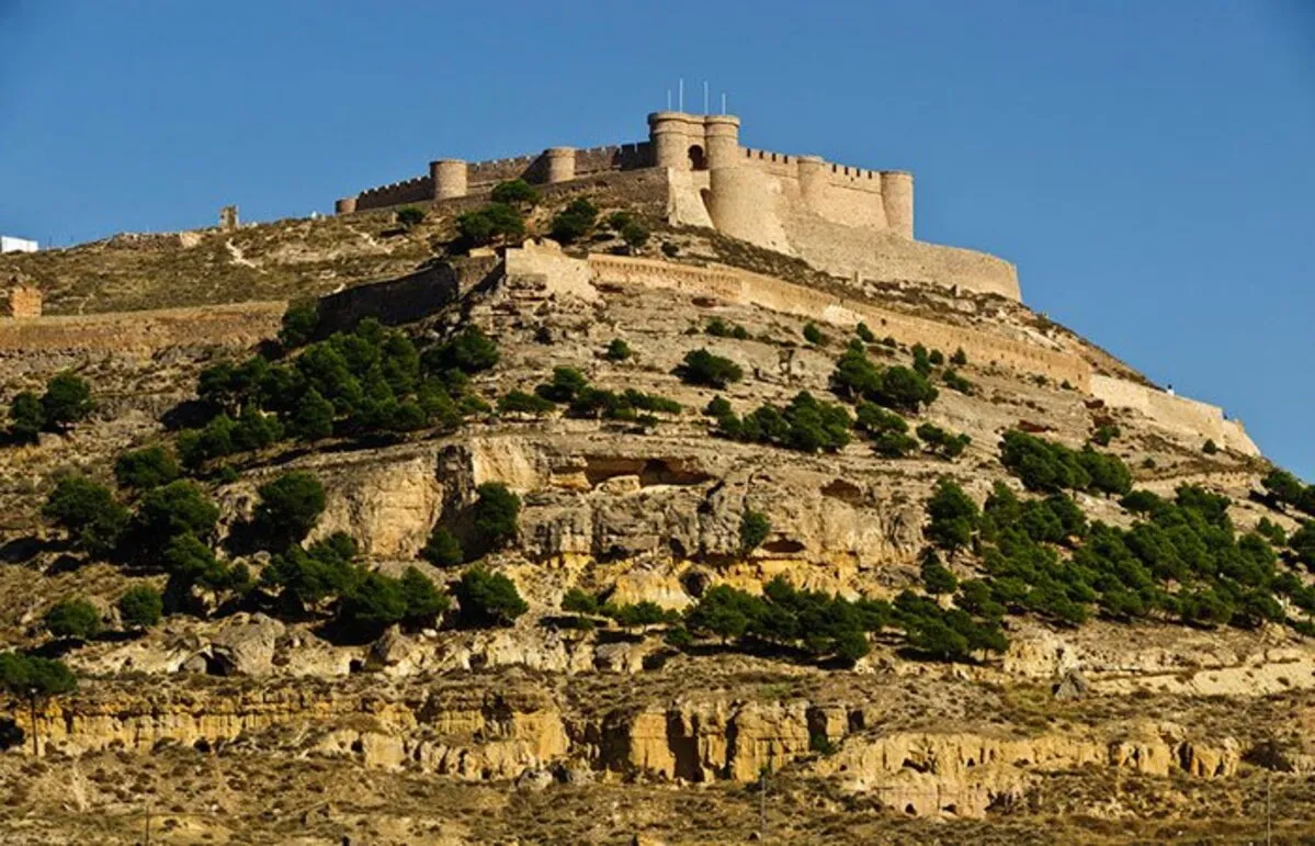 Un gran castillo medieval y una muralla sobre un monte rocoso