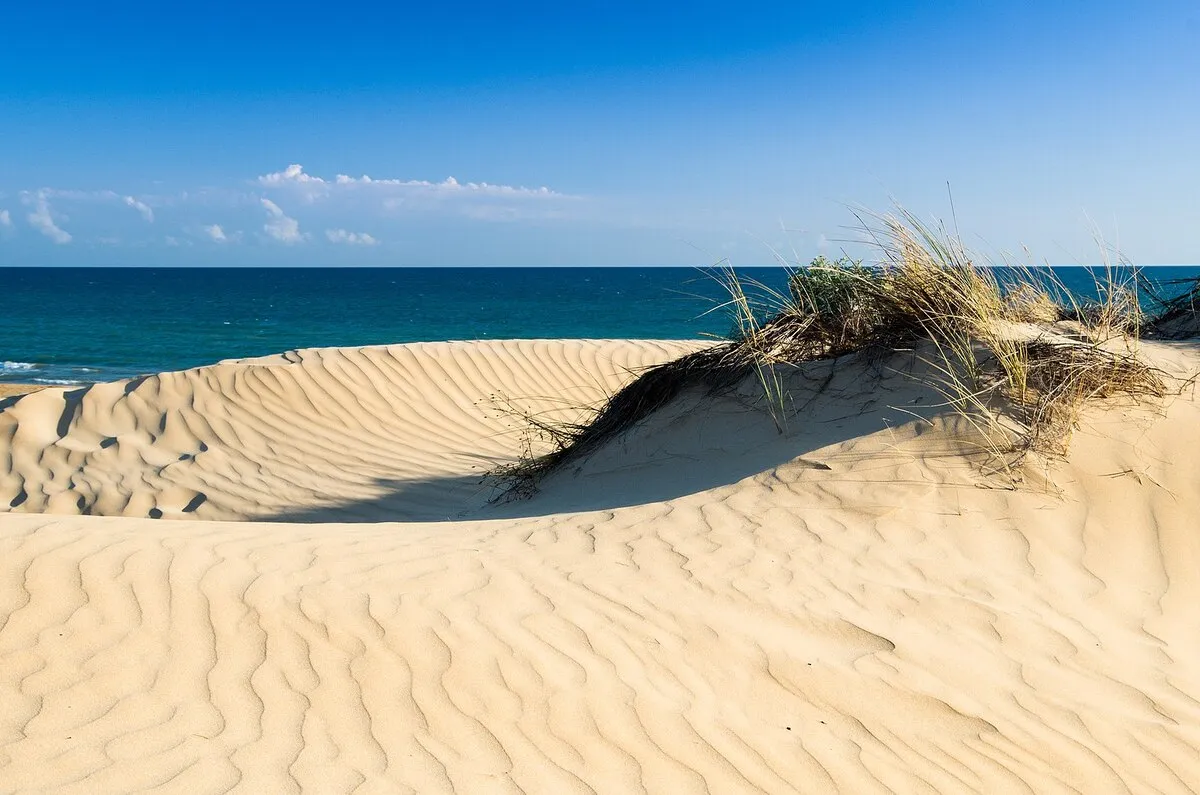 Una de las dunas de arena blanca de la playa con el agua azul turquesa de fondo