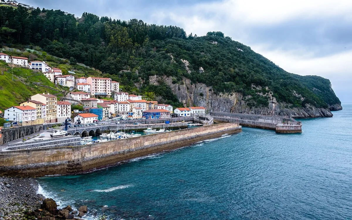 El puerto del pueblo rodeado por un muro de piedra que lo separa del mar cantábrico. En el fondo están las casas