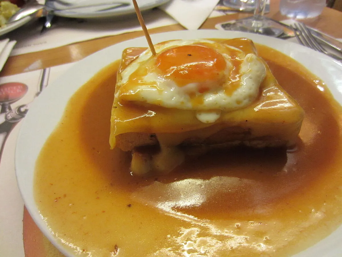 Plato de Francesinha con un huevo frito encima del sándwich de pan de molde con carne y embutido dentro