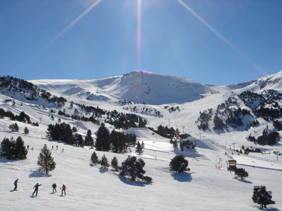 Una de las pistas principales de la estación de Andorra con arboles y personas esquiando