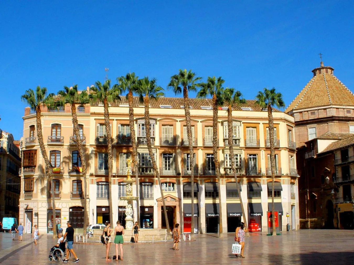 La fuente de la plaza y las palmeras de fondo frente a uno de los edificios neoclásicos del centro de la ciudad