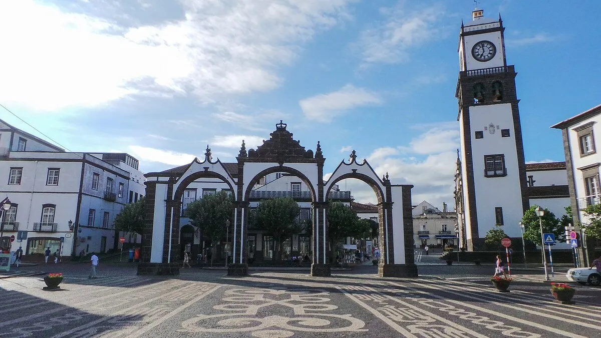 Los tres arcos blancos con detalles de ladrillo oscuro en las esquinas con la torre De la Iglesia de fondo