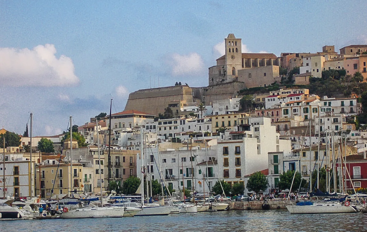 Una panoramica del puerto de Ibiza repleto de barcos de vela y el famoso castillo medieval de fondo