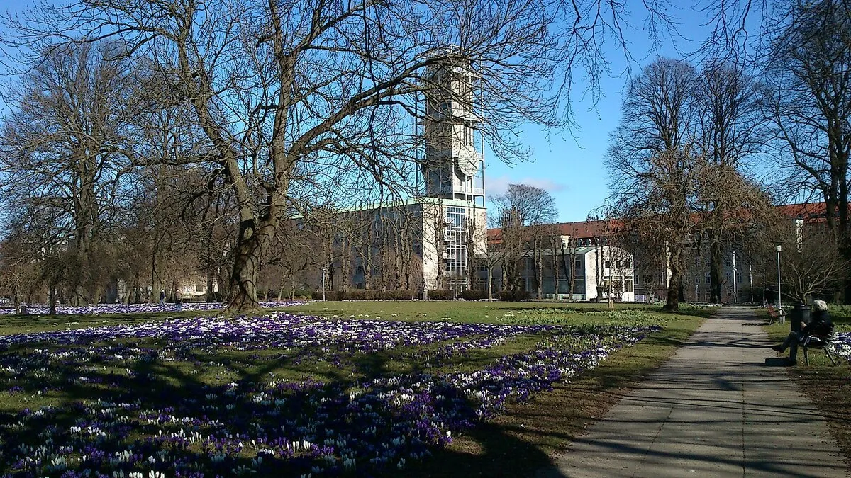 Una panorámica del edificio del ayuntamiento desde el parque con flore moradas y blancas que hay justo al lado