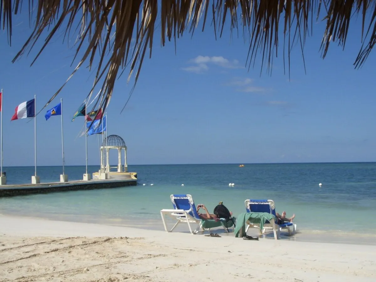 Dos personas tomando el sol en una hamaca en la ordilla de la playa con arena blanca y agua color turquesa