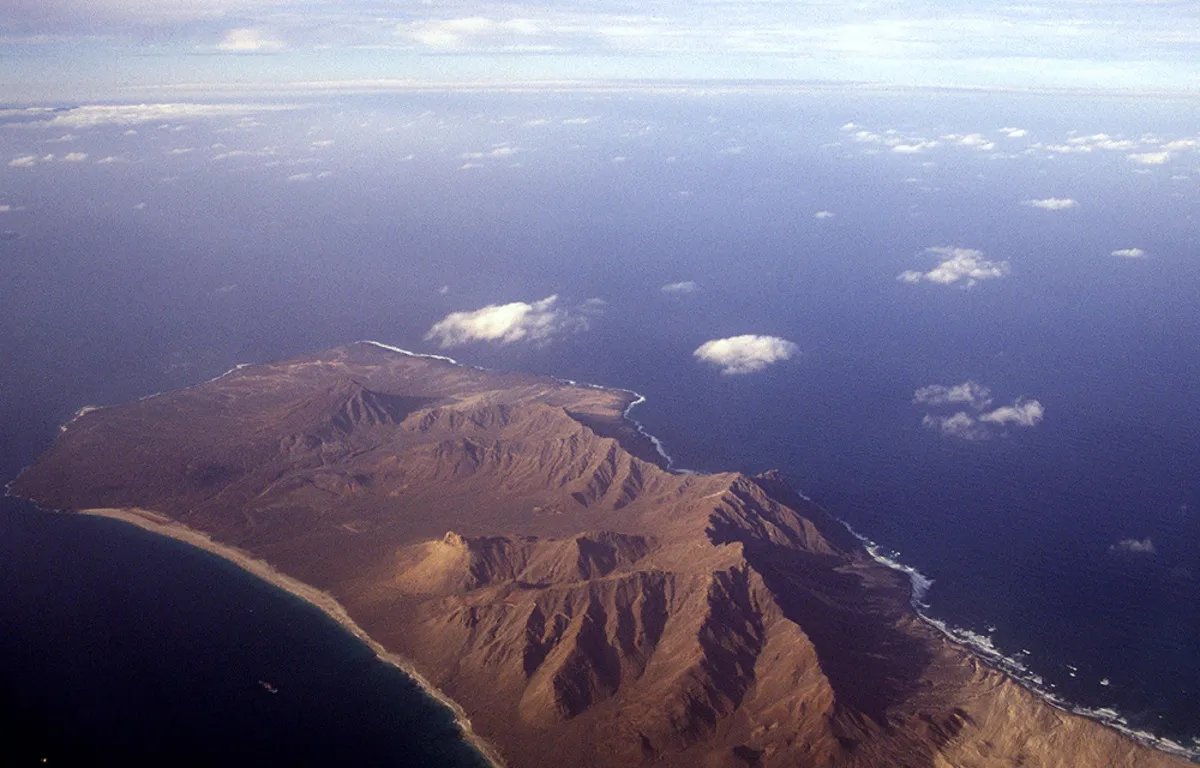 Panorámica de la isla desde el cielo con montañas de arena volcánica y el mar