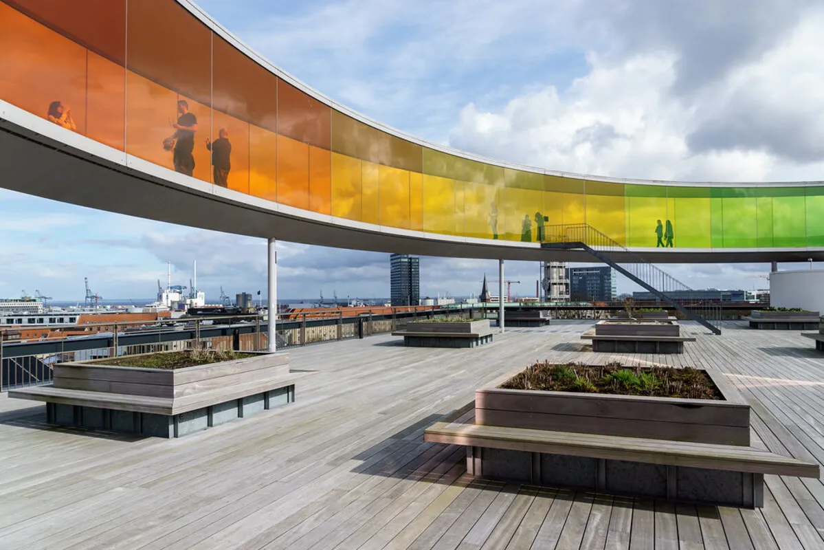 La terraza panorámica y multicolor del museo con gente paseando por ella y asientos cuadrados de madera con plantas