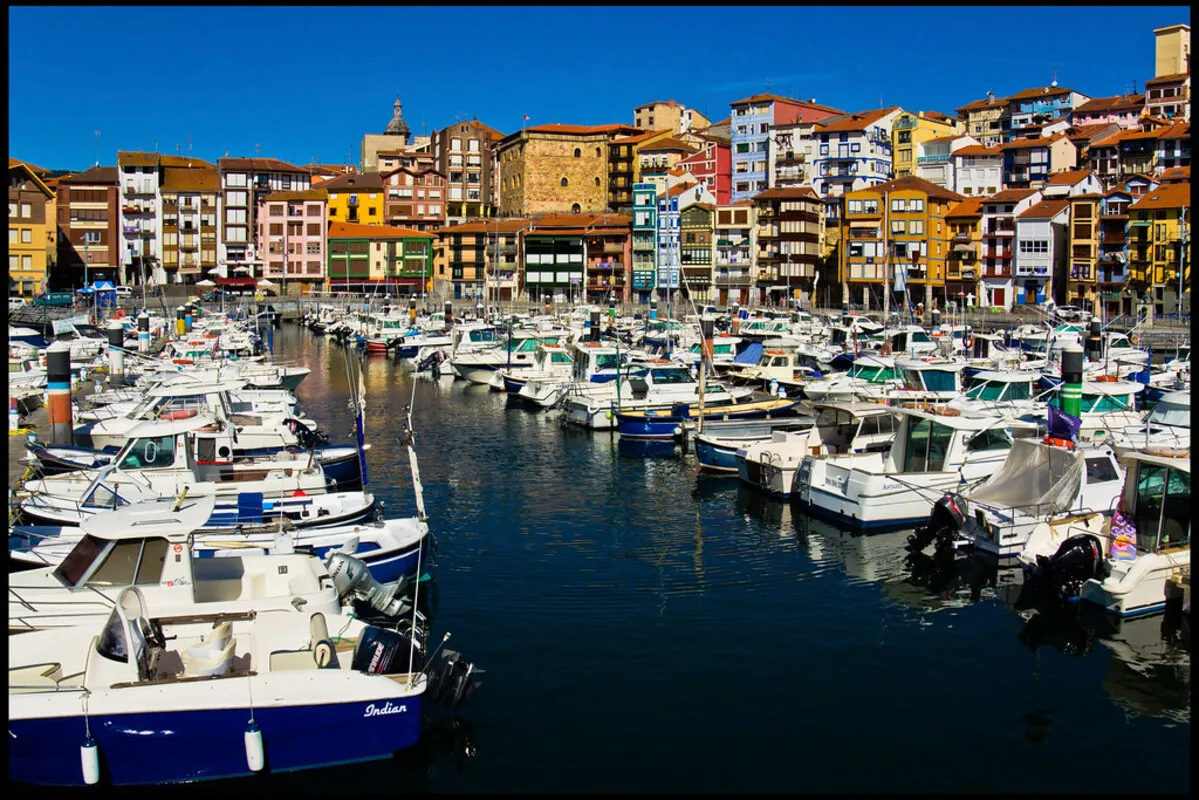 Panorámica del puerto del pueblo con las casas de colores al fondo y barcos veleros anclados