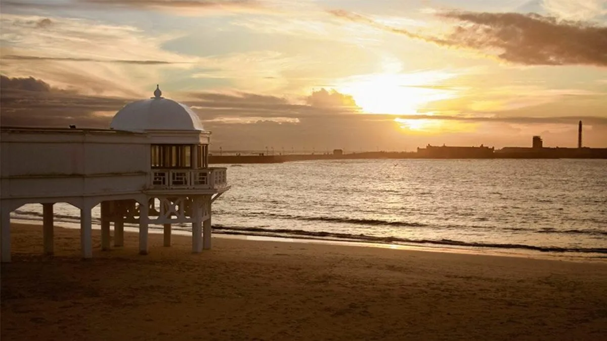 Puesta de sol en la playa de la Caleta con pasarela blanca de madera