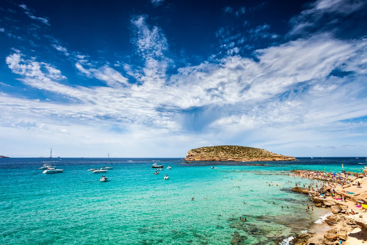 Panoramica de la cala con el agua del mar color turquesa y varios barcos de vela durante un día soledado