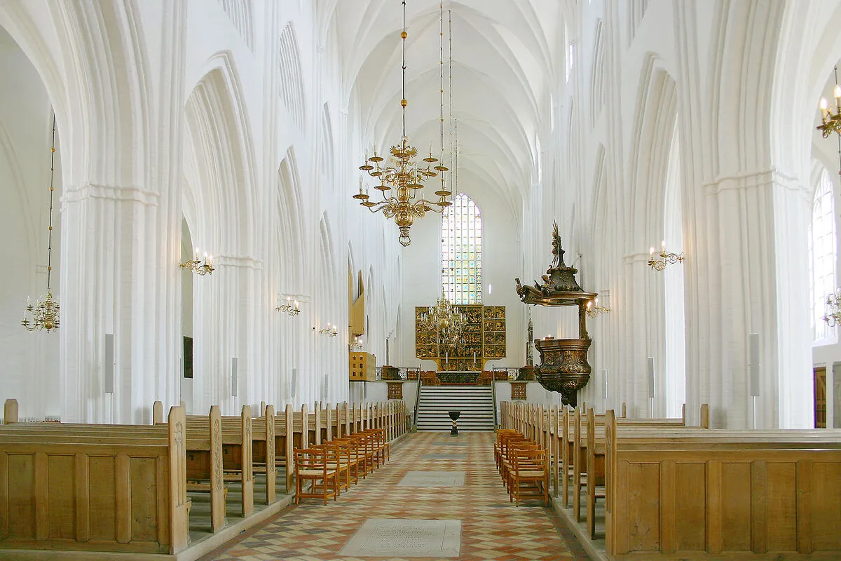 El interior de la catedral con los asientos de madera, los arcos de medio punto blancos y el retablo de madera al fondo
