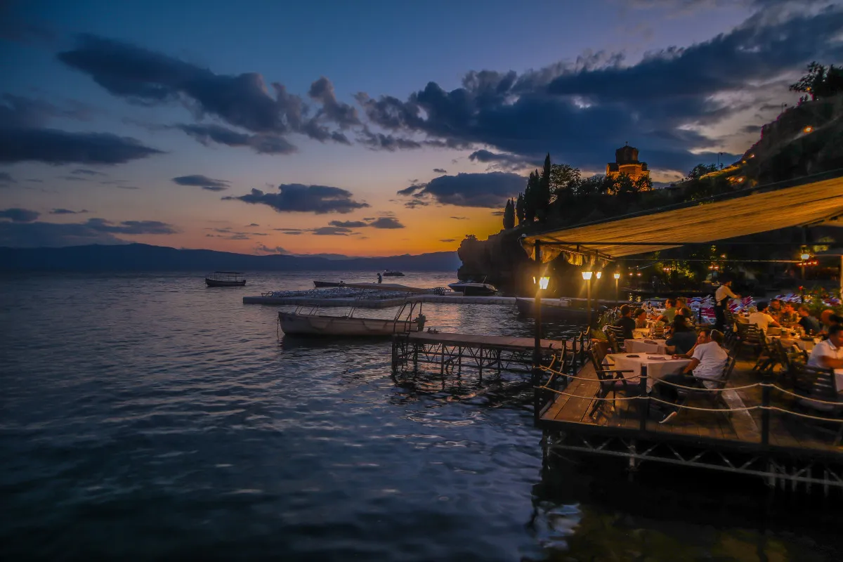 El lago Ohrid por la noche con gente cenando en uno de los restaurantes que se encuentran en la pasarela de madera