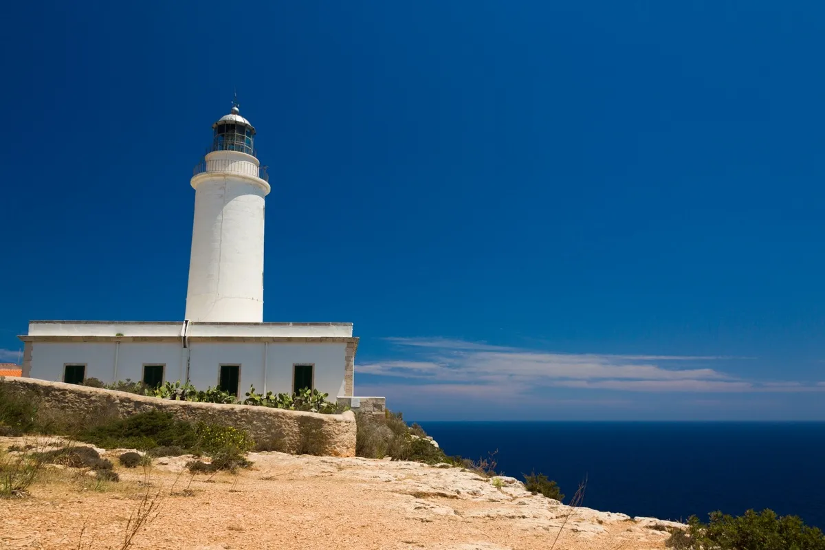 Una panorámica del faro con el agua de fondo y el acantilado, durante un día soleado y despejado de nubes