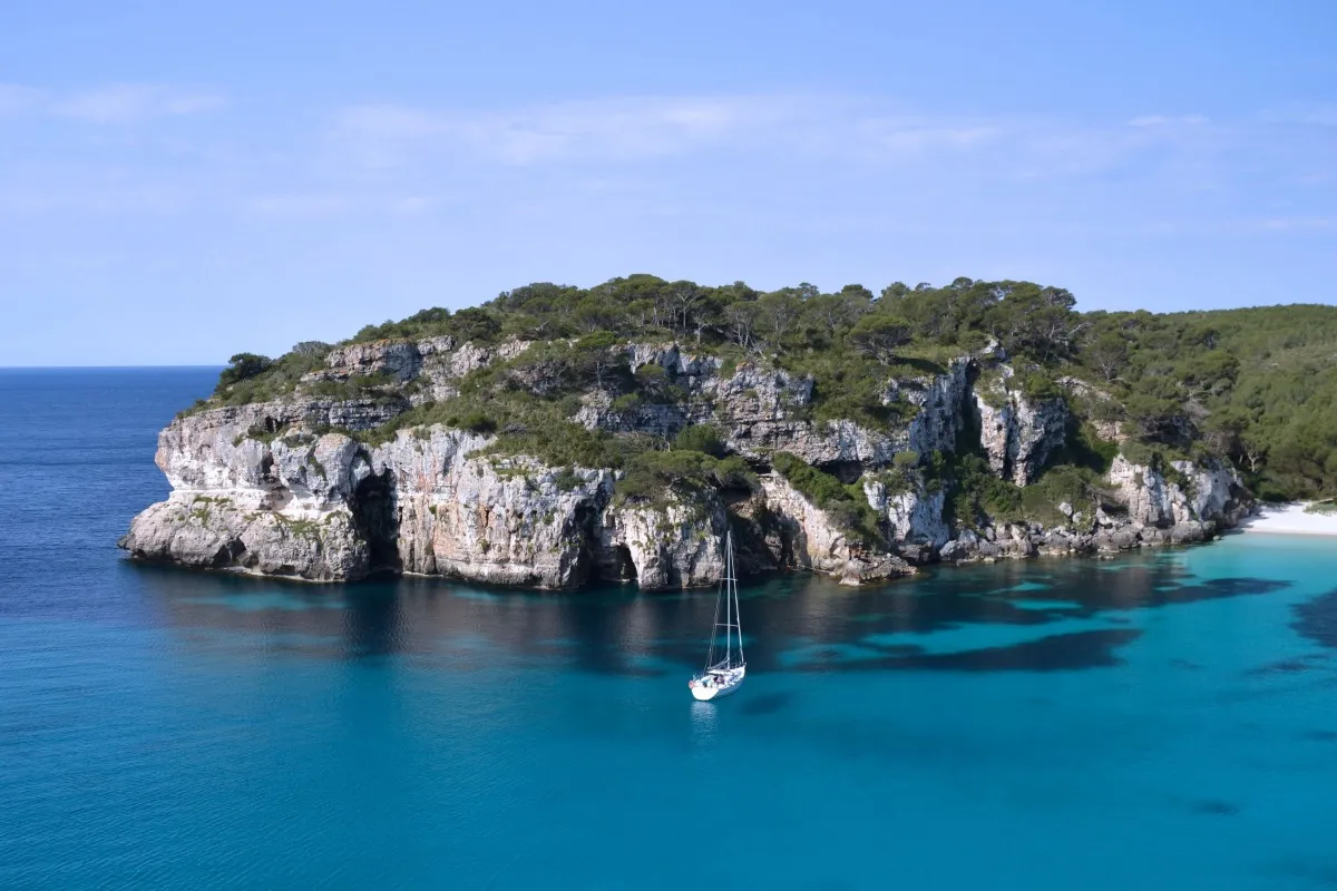 Una panorámica de la isla con acantilados y un barco velero llegando a la orilla