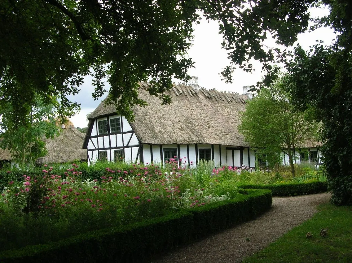 Una de las casas recreadas de color blanco y con tejado de paja. La casa esta rodeada de flores y arboles