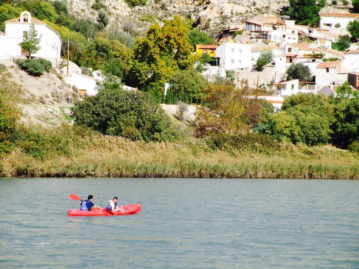 dos personas montadas en kayak por el rio jugar pasando por unas casas de pueblo blancas