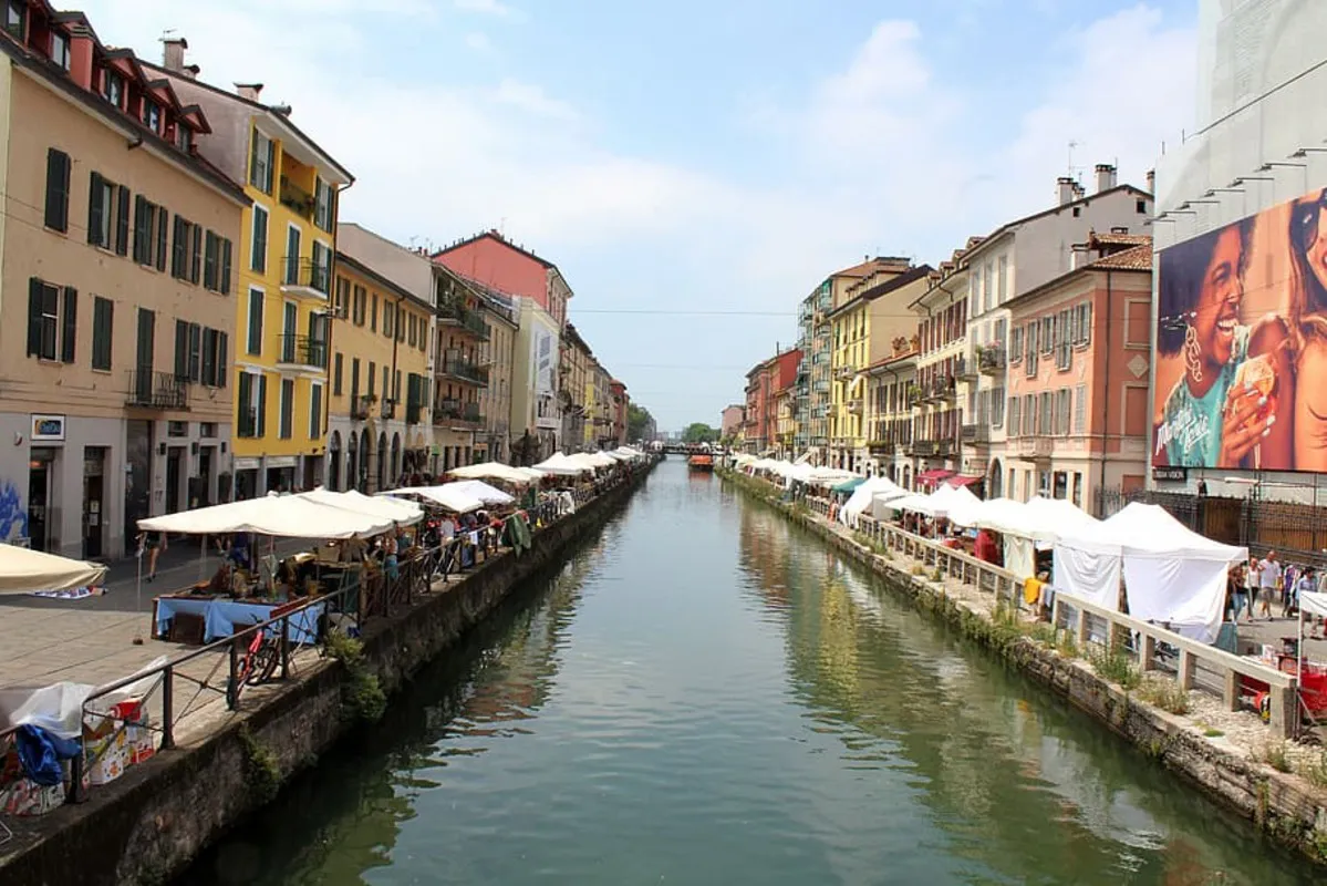 El famoso canal del barrio de Navigli de día con bares y restaurantes a los lados y uno de los barcos que cruzan el canal