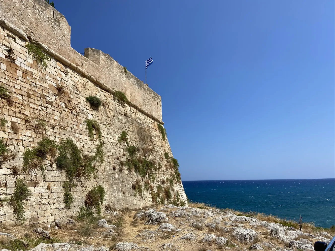 Muralla de la fortaleza desde el exterior con la bandera griega ondeando.