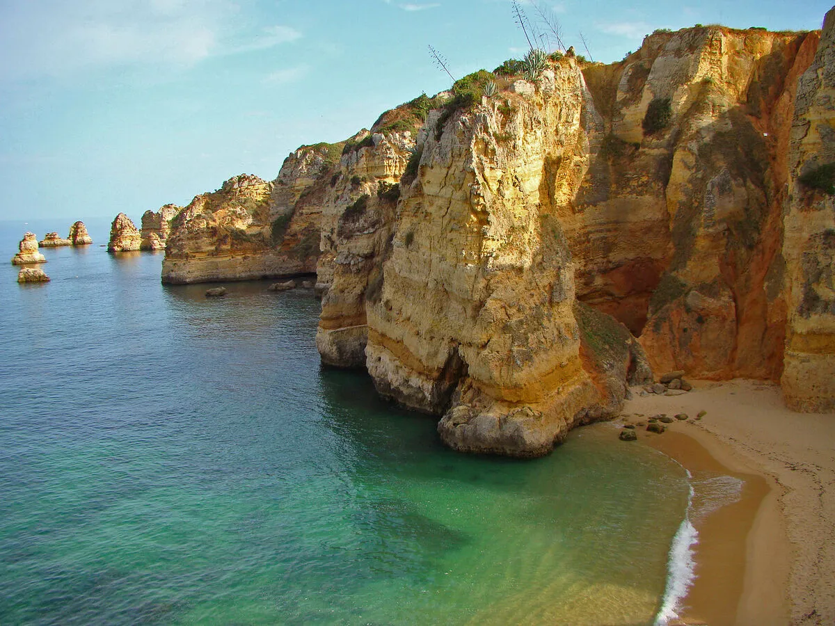 Panorámica de la playa desde arriba con el agua de color verdoso y las formaciones rocosas en la orilla de la pequeña cala
