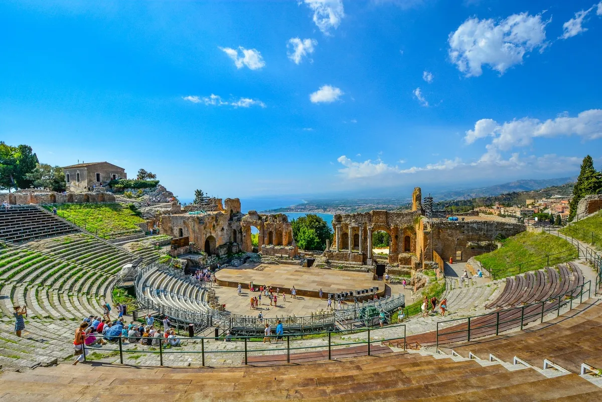 Panorámica del teatro griego desde uno de los escalones más altos con el mar de fondo y la ciudad